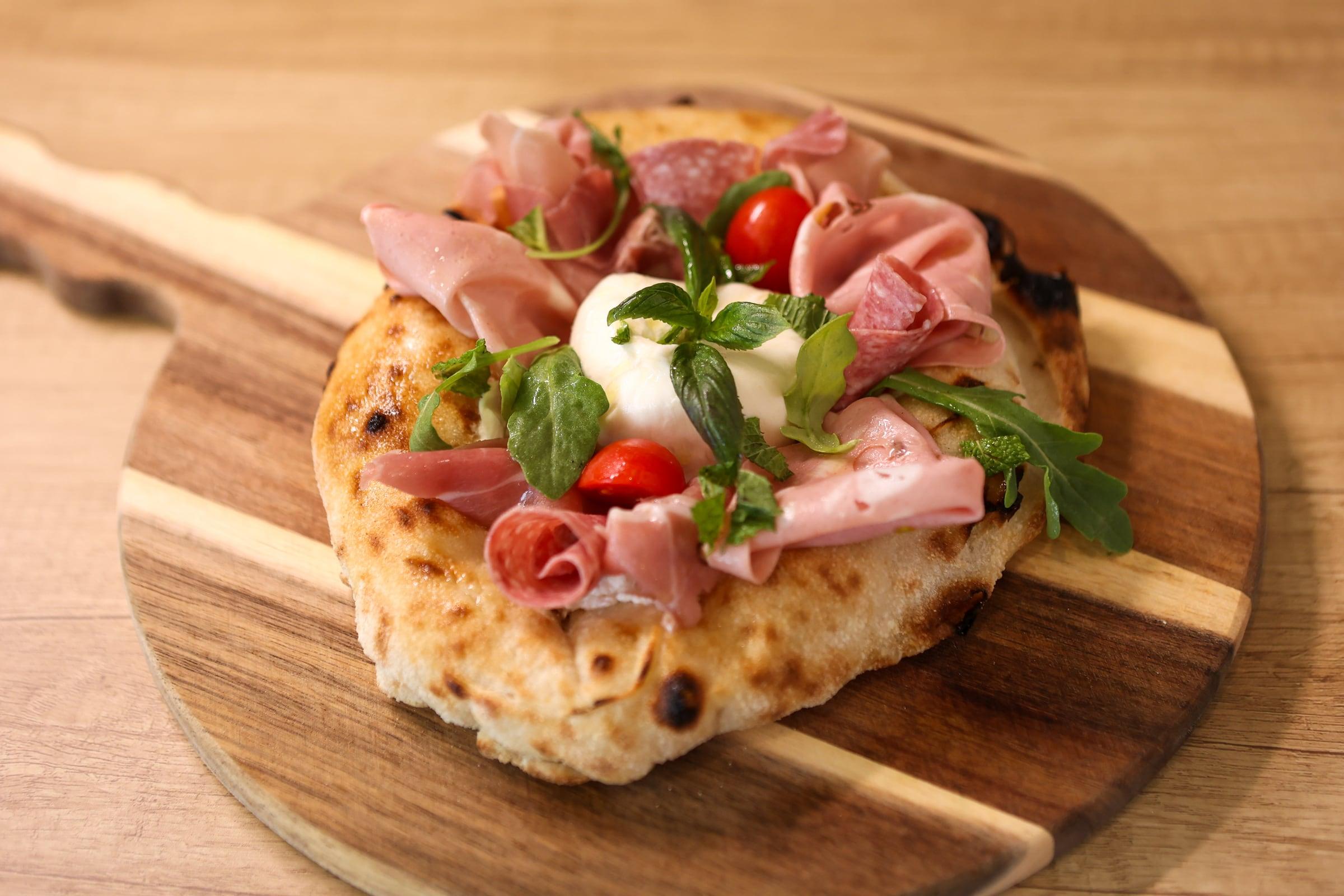 Crust Nova fire-baked pizza with burrata, cured meats, tomatoes and fresh greens